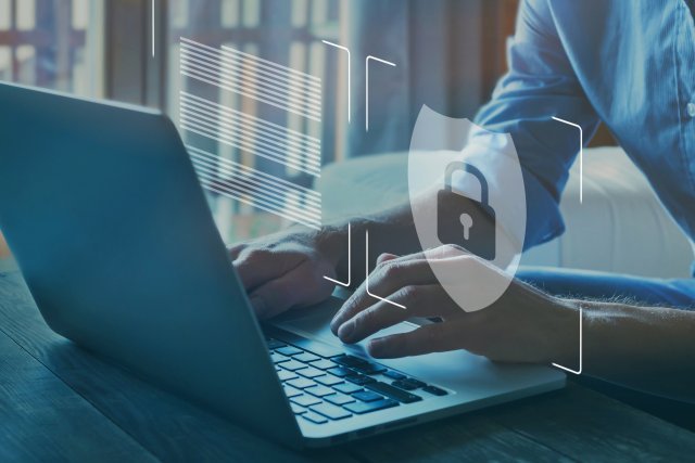 Padlock and shield superimposed over a closeup of man's hands typing on a laptop